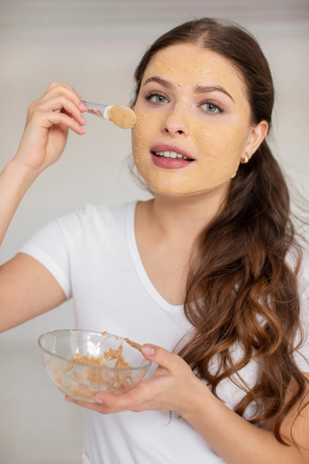 A woman applying a turmeric paste to her face from a glass bowl