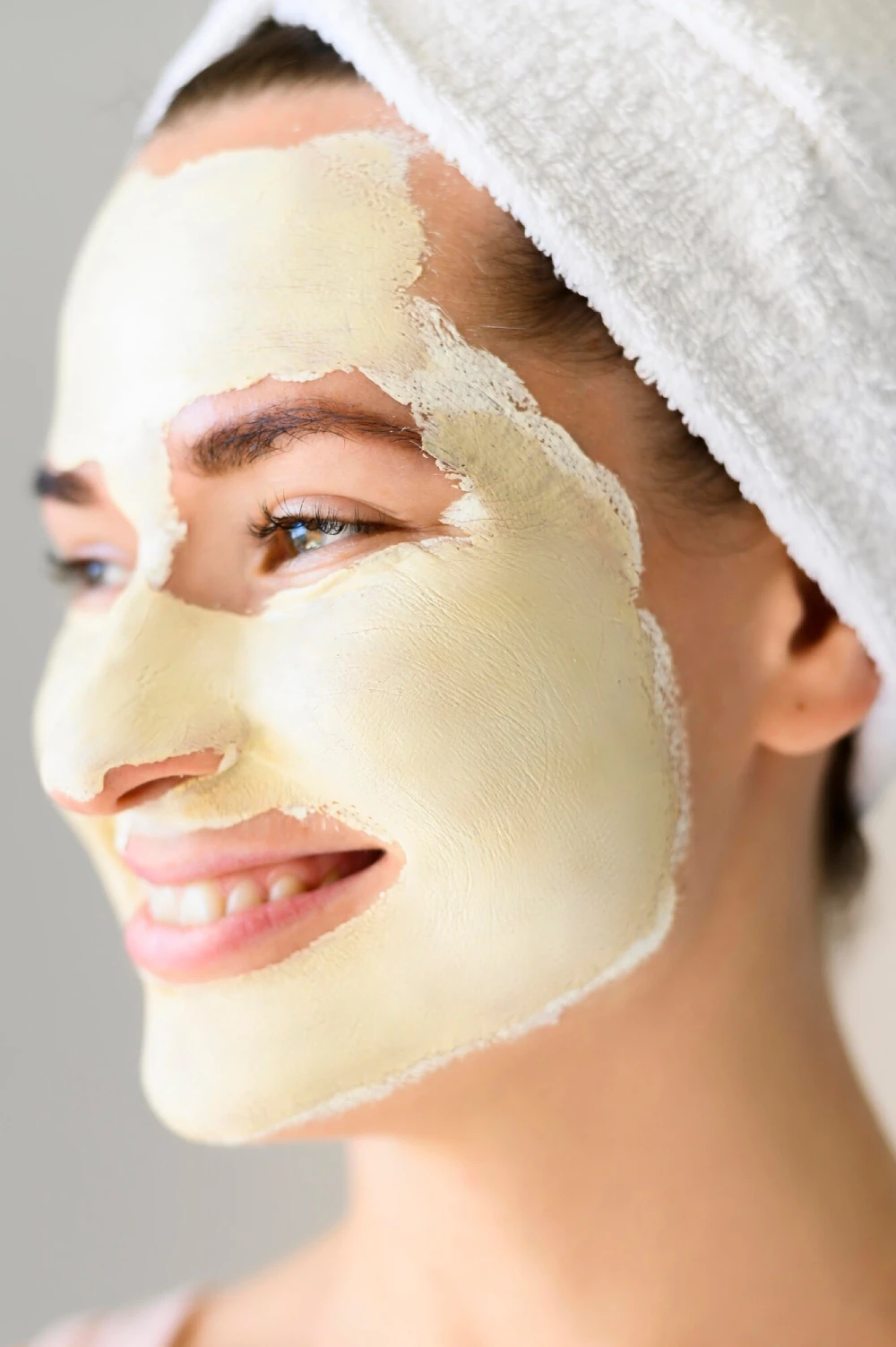 A smiling woman in a towel wrap with a creamy yoghurt mask