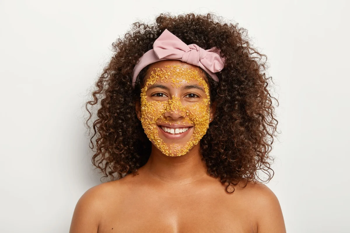 A smiling woman with a golden turmeric scrub on her face