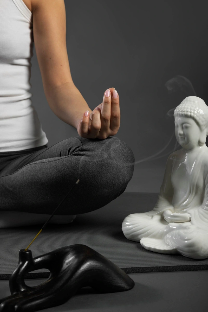 A meditator in a hand mudra beside a white Buddha statue and incense