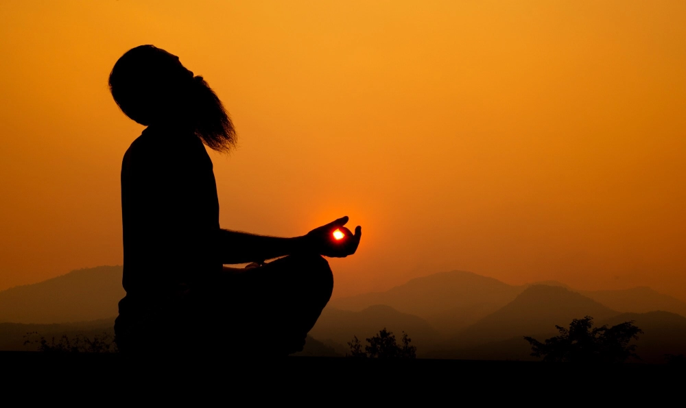 The silhouette of a meditator against an orange sunset over the hills