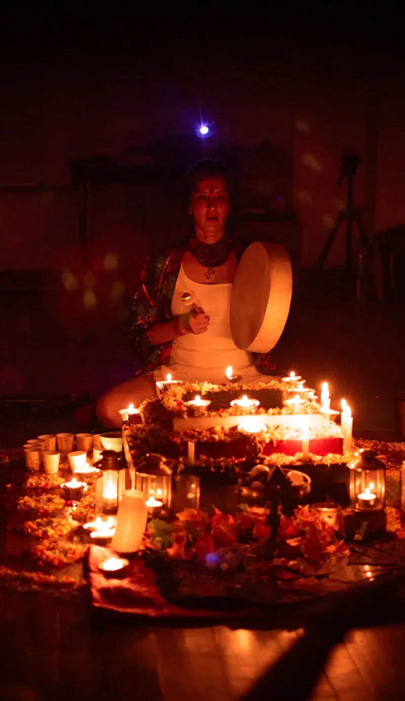 A facilitator singing with a frame drum beside a candlelit cacao altar