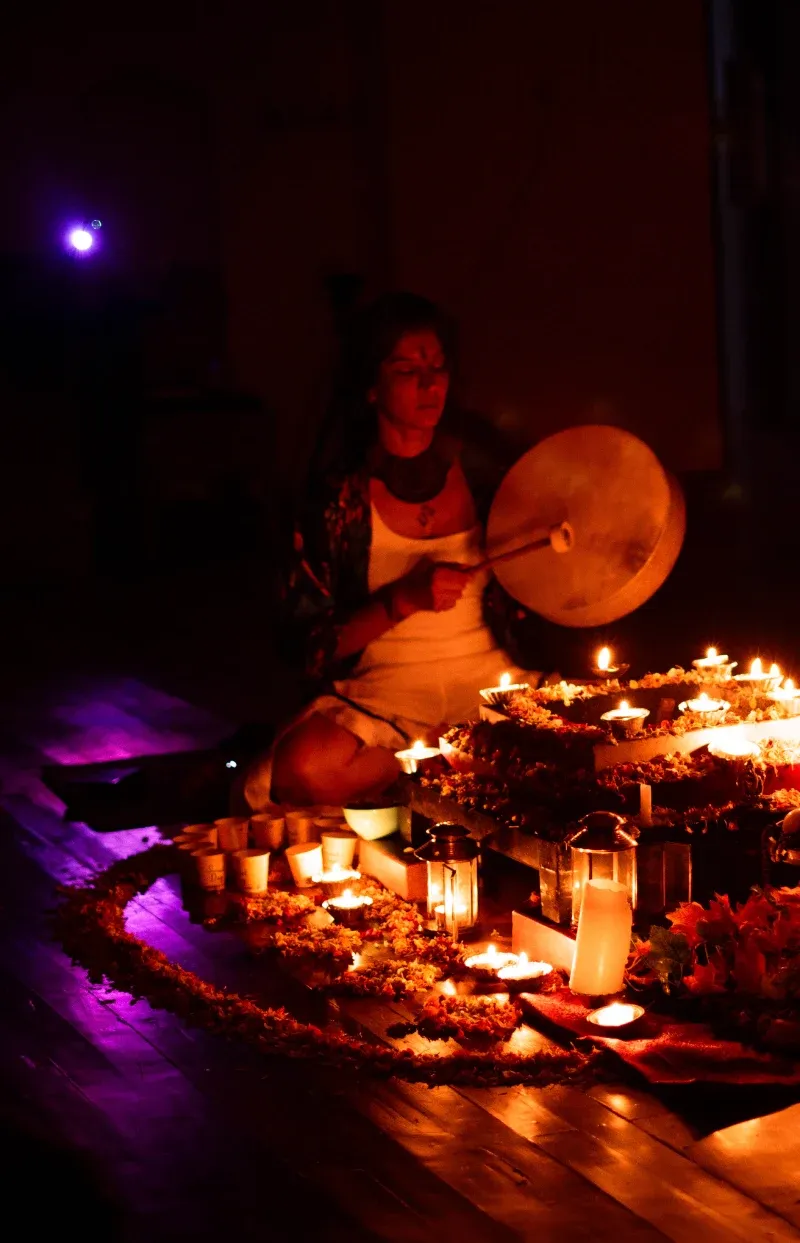 A facilitator drumming beside a flower and candle mandala