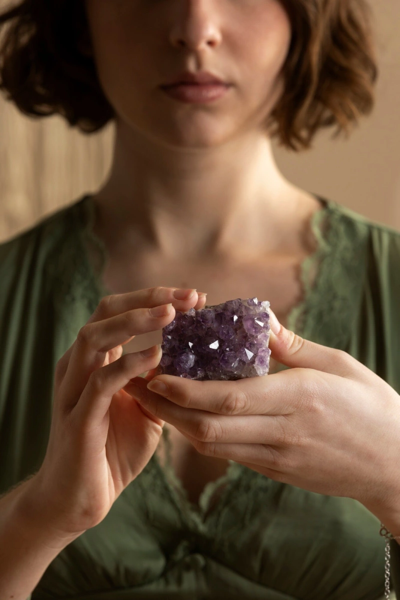 A woman holding an amethyst cluster in both hands at her chest