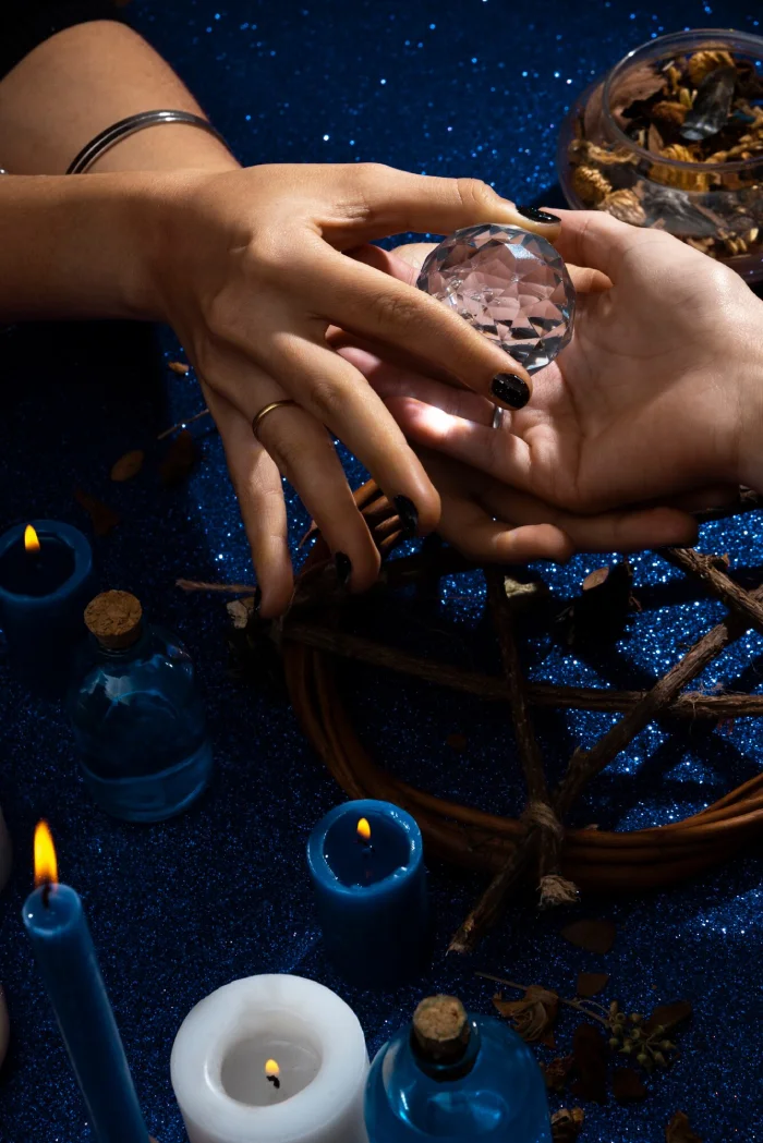 A healer placing a clear crystal in another person’s open palm beside lit candles