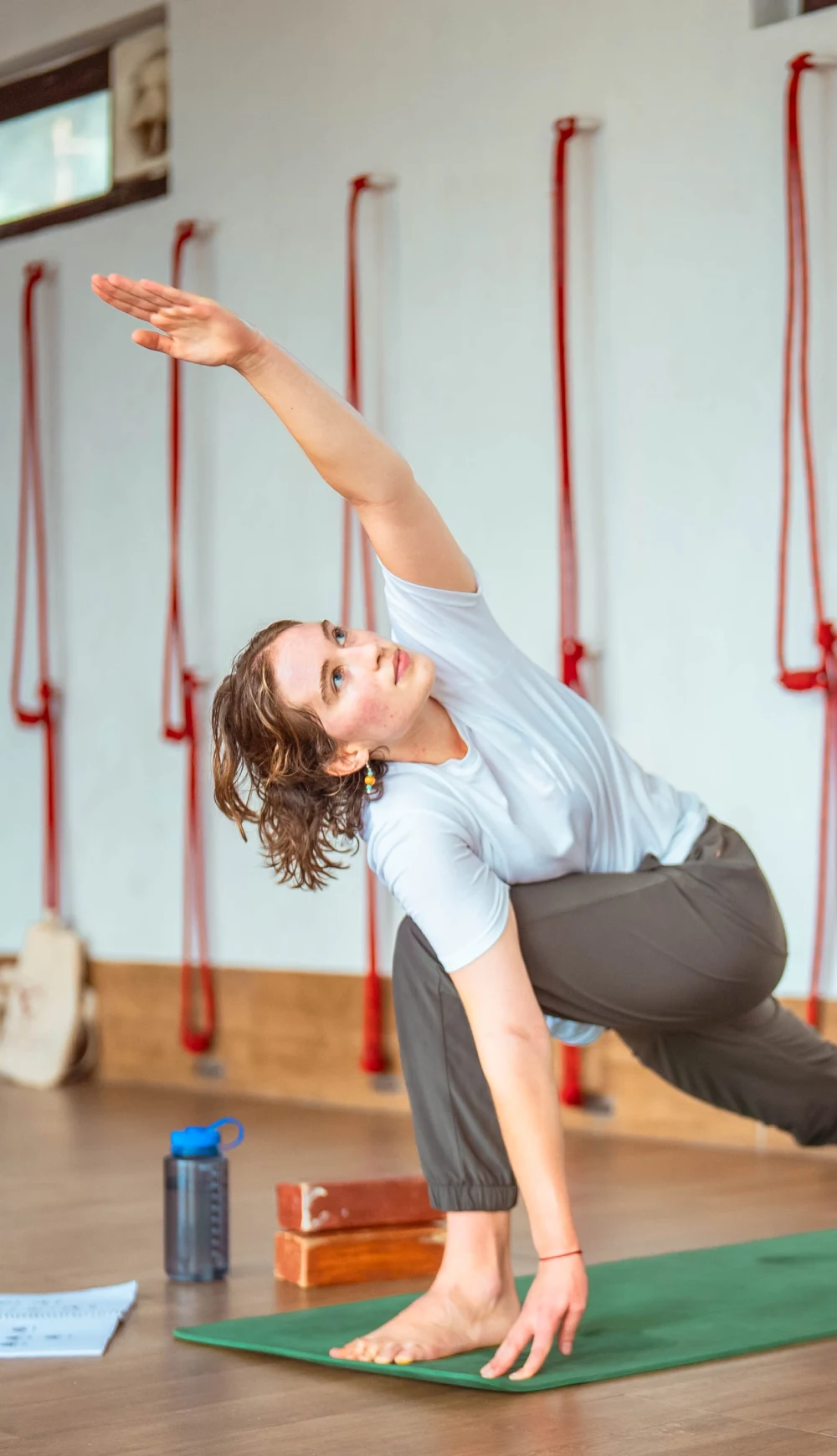 A woman in an extended side angle pose in a studio with wall ropes