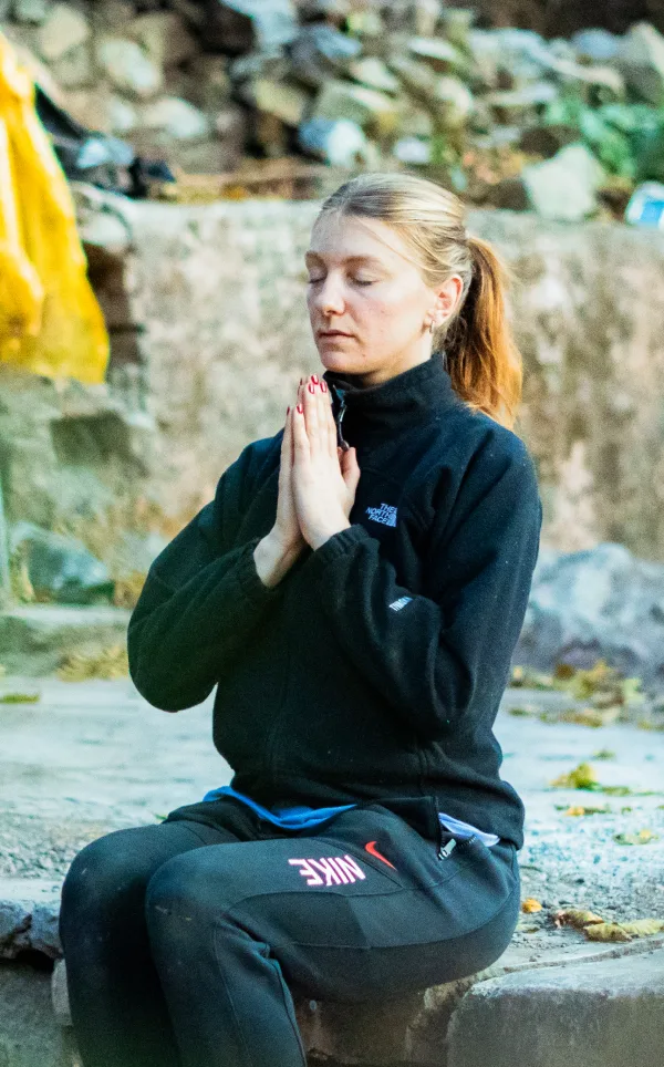 A woman meditating with palms joined on a stone ledge