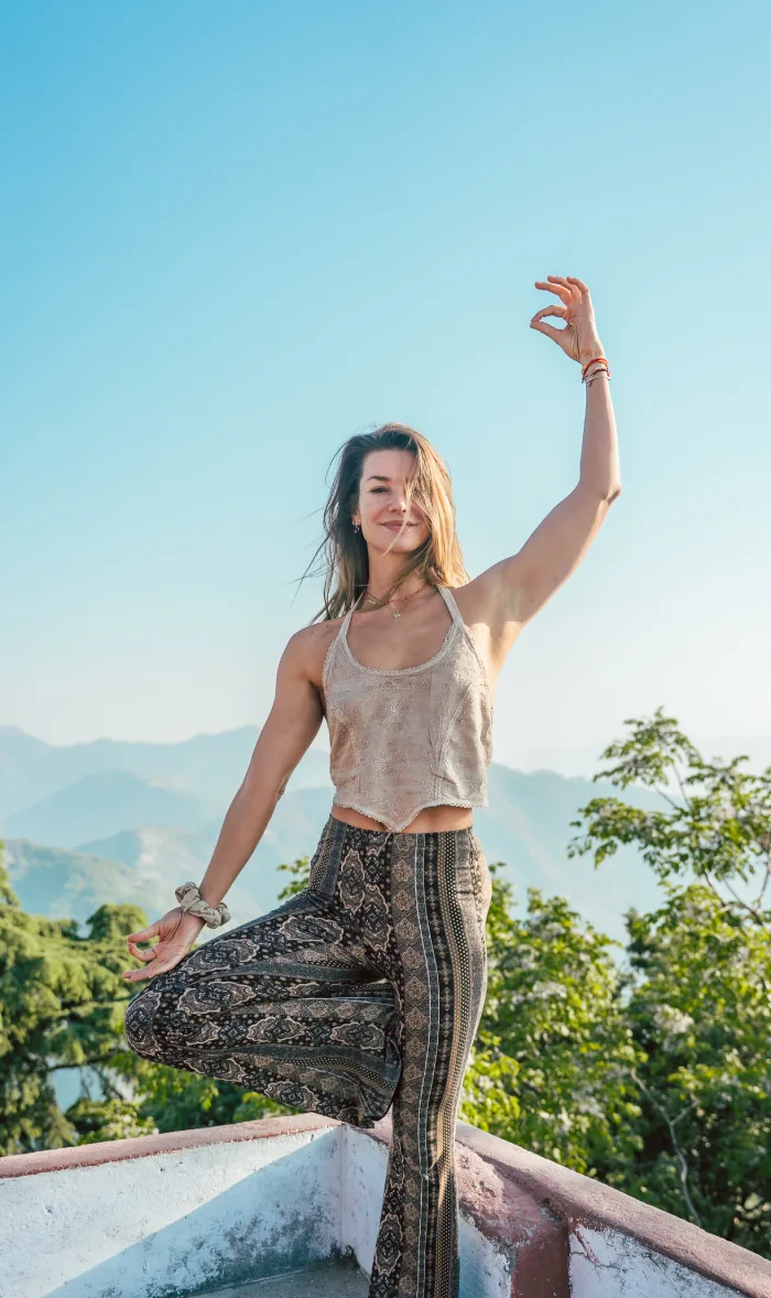 A smiling woman balancing on one leg on a rooftop above the hills
