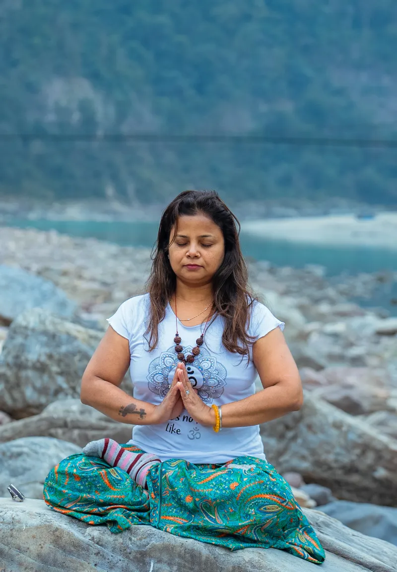 A woman meditating with palms joined on a rock by the Ganges