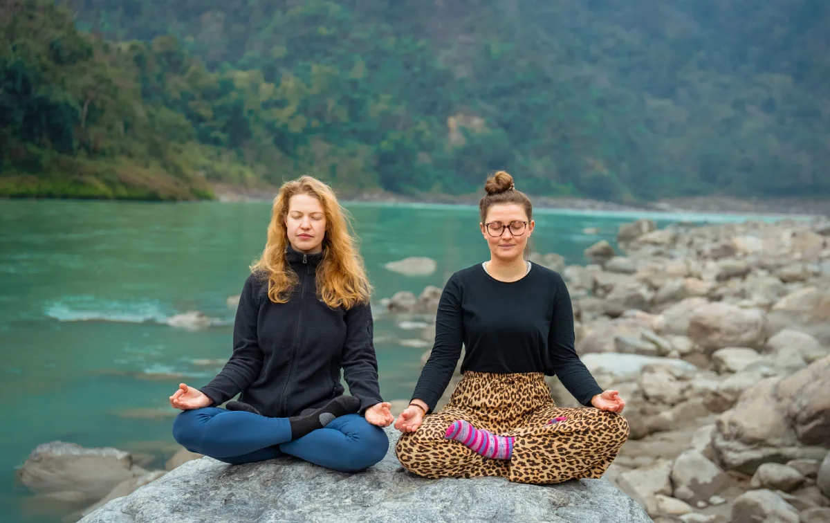 Two women meditating side by side on a rock by the Ganges