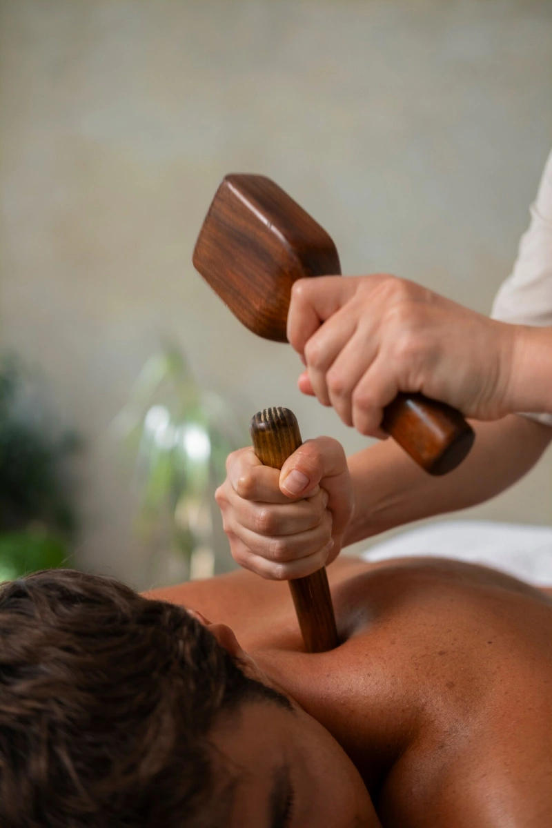 A therapist using wooden massage tools on a guest’s shoulder