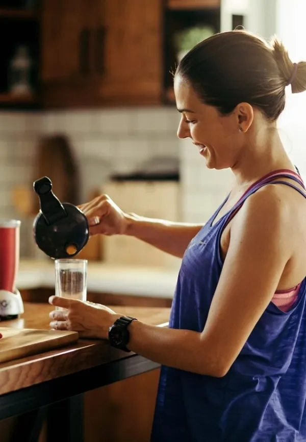 A smiling woman pouring a green smoothie in her kitchen