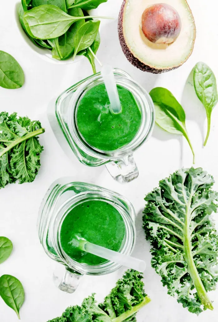Green smoothies surrounded by kale, spinach, and avocado