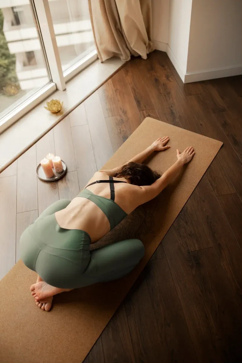 A woman resting in child’s pose on a cork yoga mat