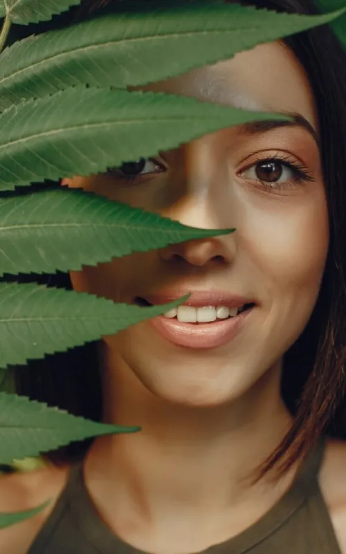 A smiling woman peeking through fresh green leaves