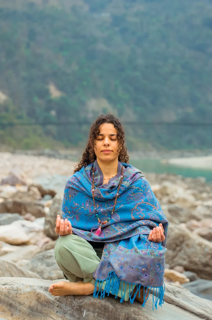 A woman wrapped in a blue shawl meditating on a rock by the Ganges