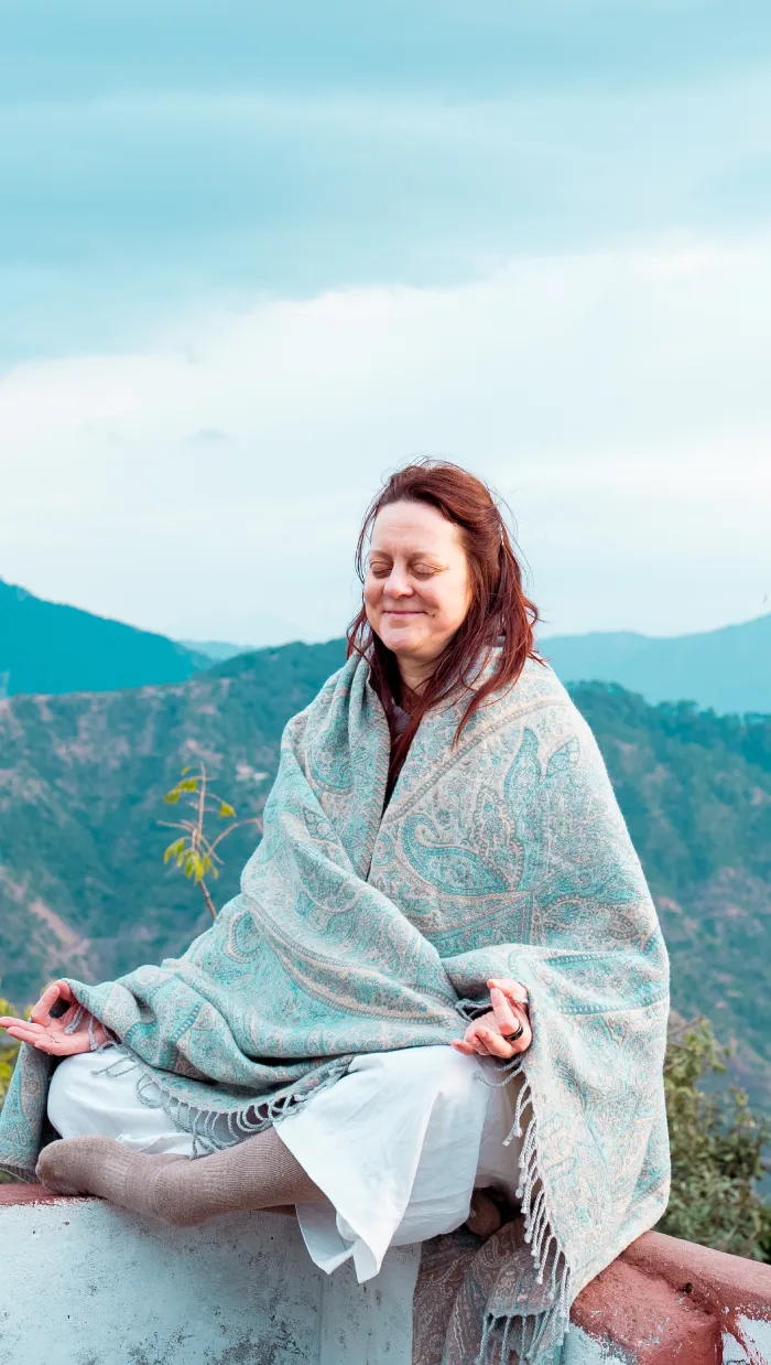 A smiling woman in a shawl meditating on a wall above the hills