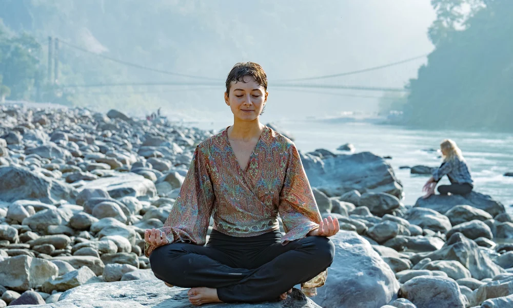 A woman meditating on the rocks of the Ganges near Rishikesh