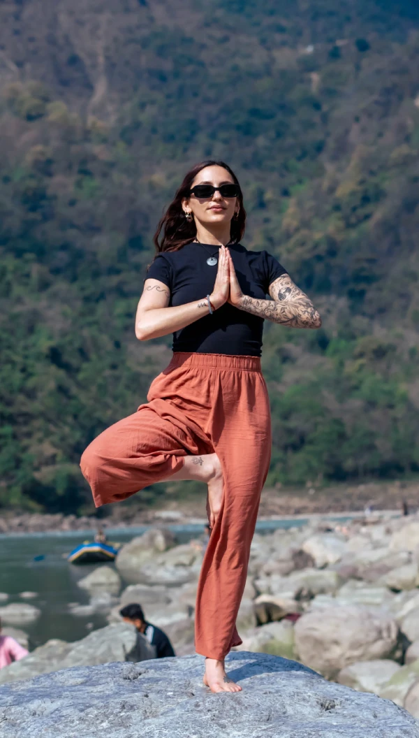 A woman in tree pose on a rock by the Ganges with hills behind