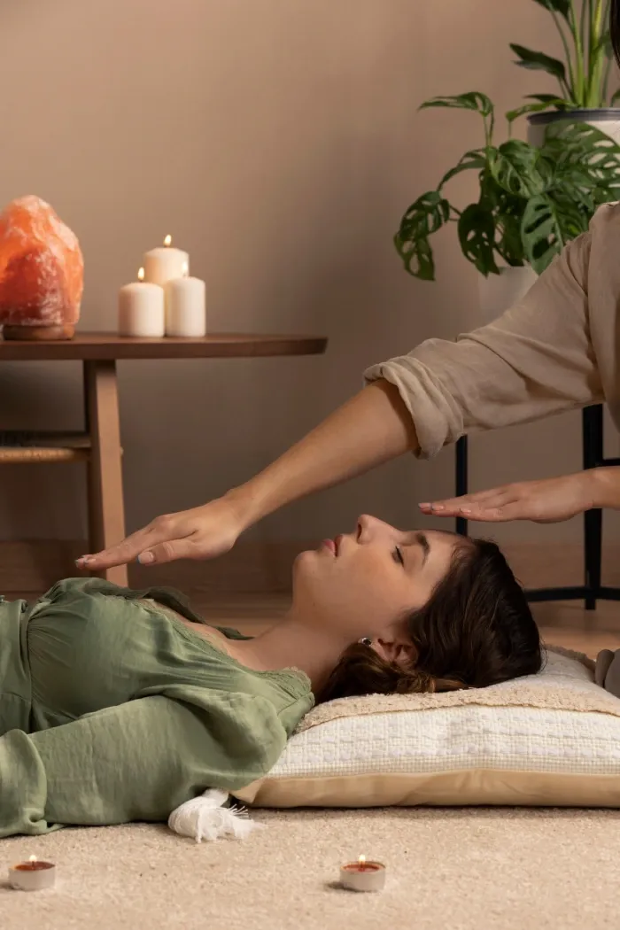A healer’s hand held over a woman resting on a cushion beside candles