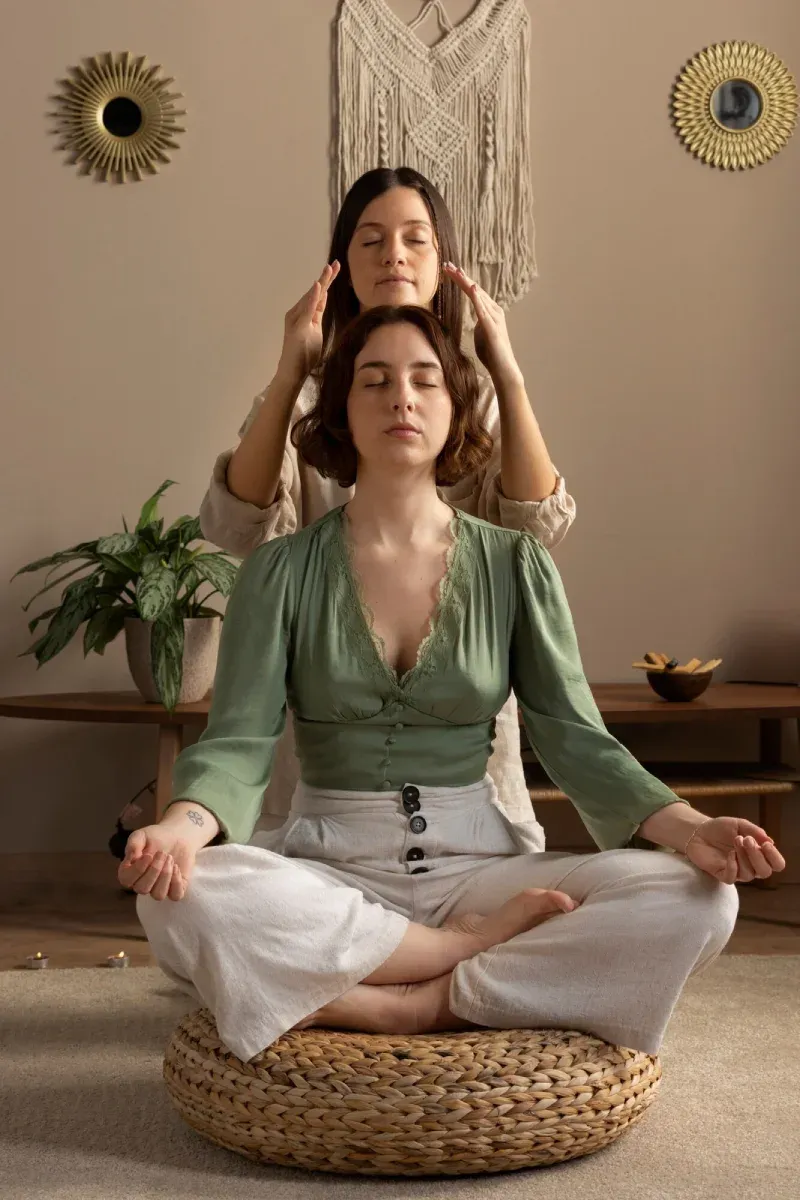 A healer’s hands above a woman meditating cross-legged