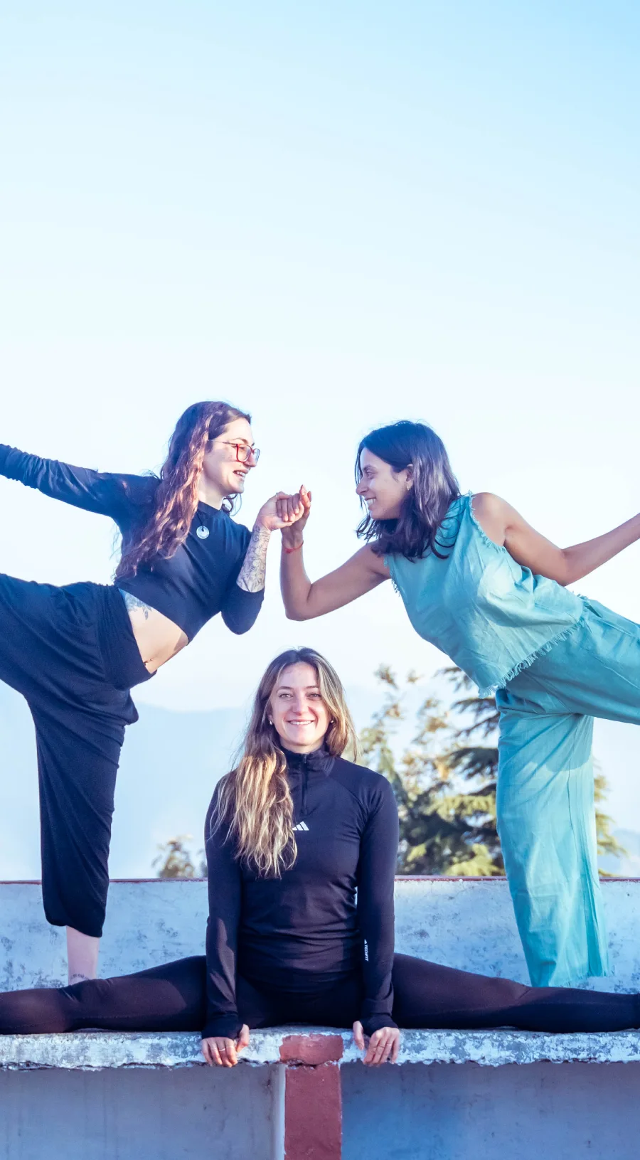 Three friends in playful balancing poses and a split on a rooftop