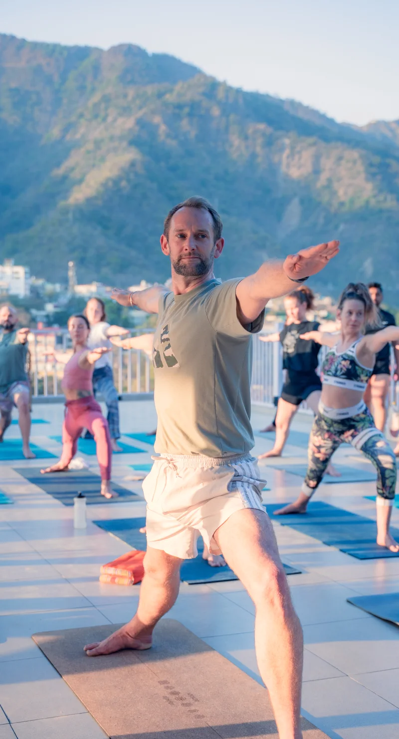 A rooftop yoga class in warrior II with hills behind