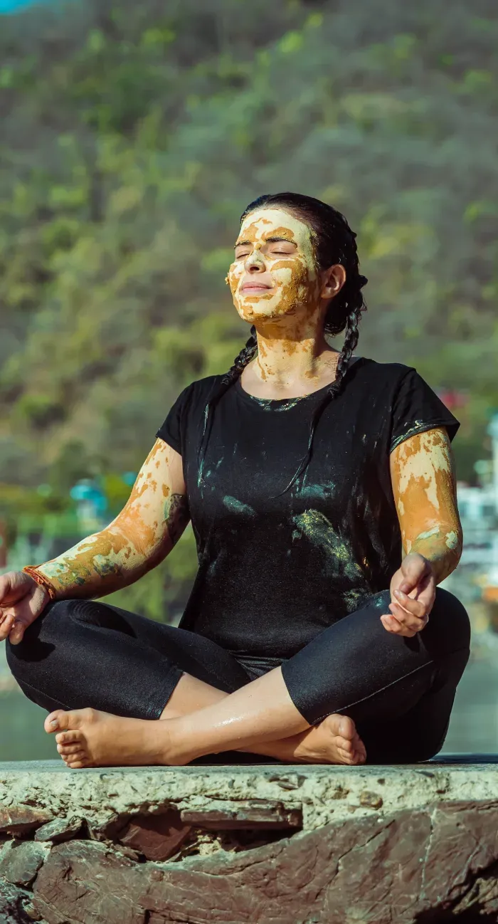 A woman covered in healing mud meditating cross-legged by the Ganges