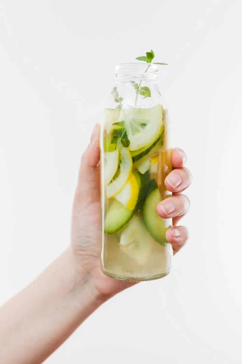 A hand holding a bottle of detox water with cucumber and lemon