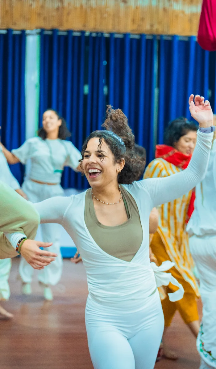 A smiling woman in white dancing freely during a group meditation