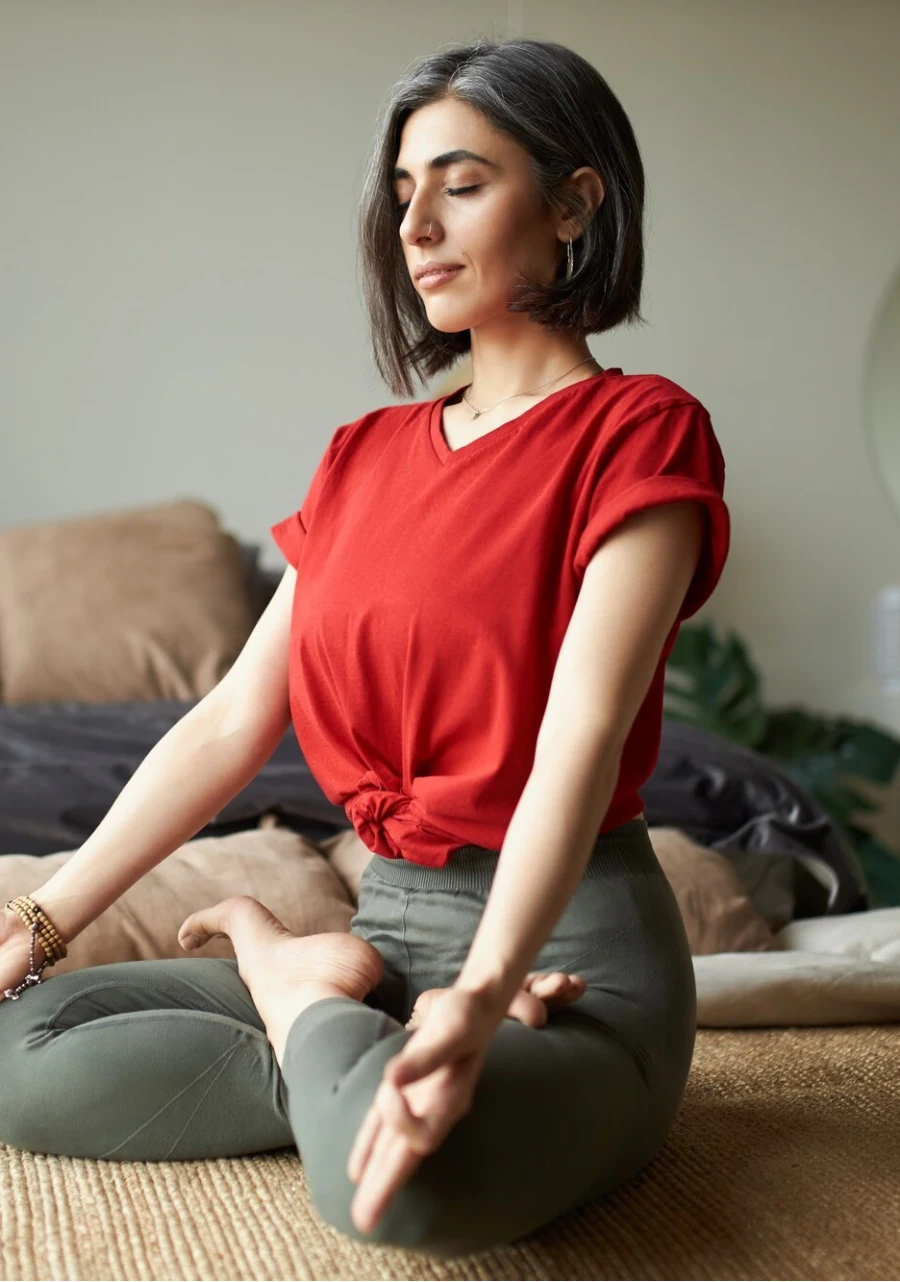 A woman seated cross-legged in meditation on a woven mat at home