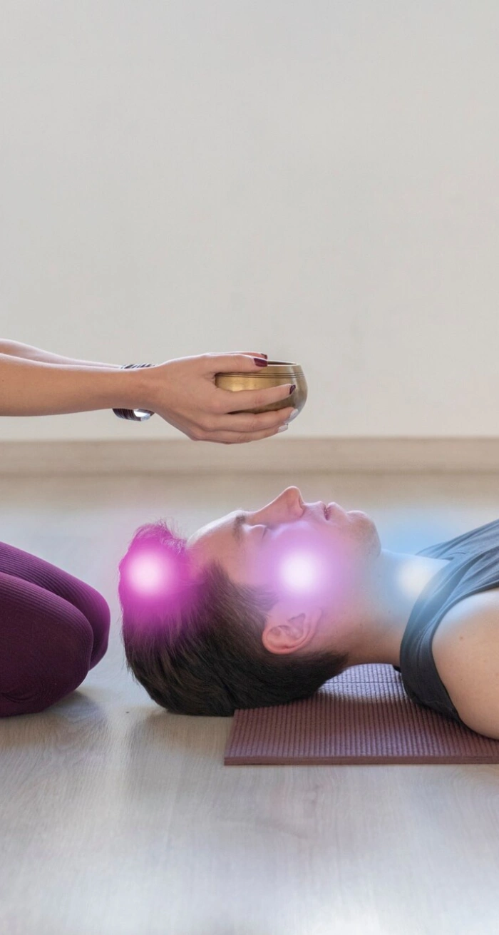 A singing bowl held above a man lying with glowing energy points at his head