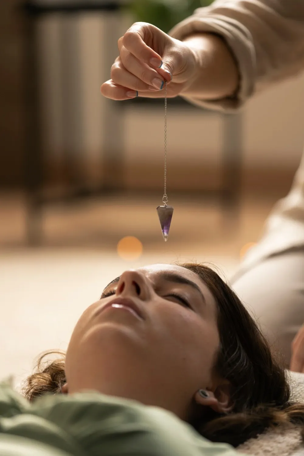 A healer holding a crystal pendulum above a resting woman
