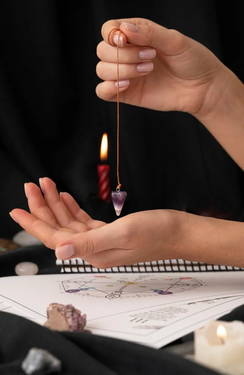 A crystal pendulum swinging over an open palm beside a candle
