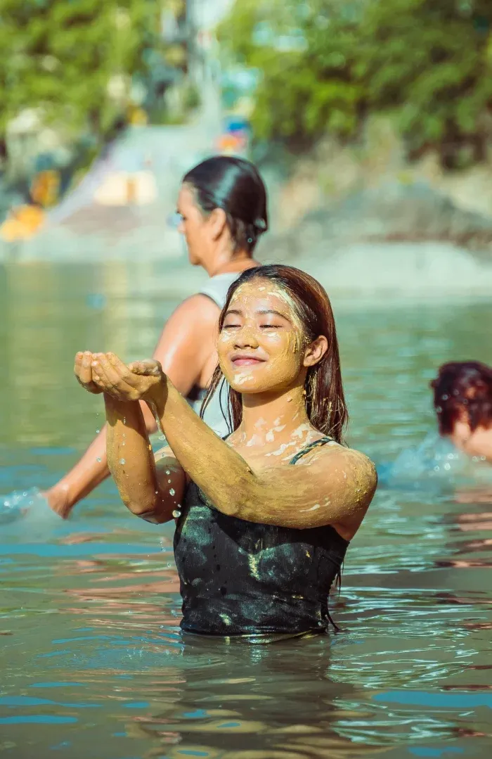 A smiling woman rinsing clay off her arms in the Ganges
