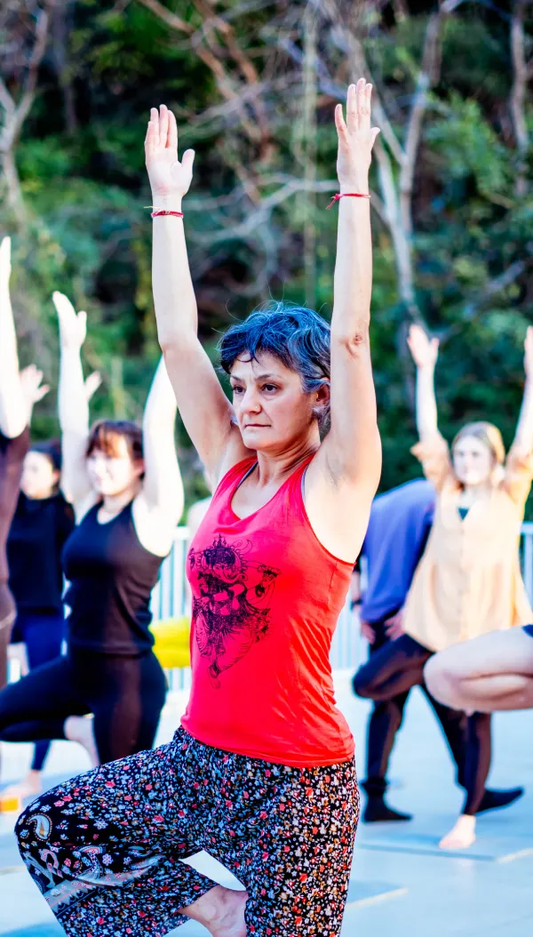 An older woman in tree pose with arms raised during an outdoor class