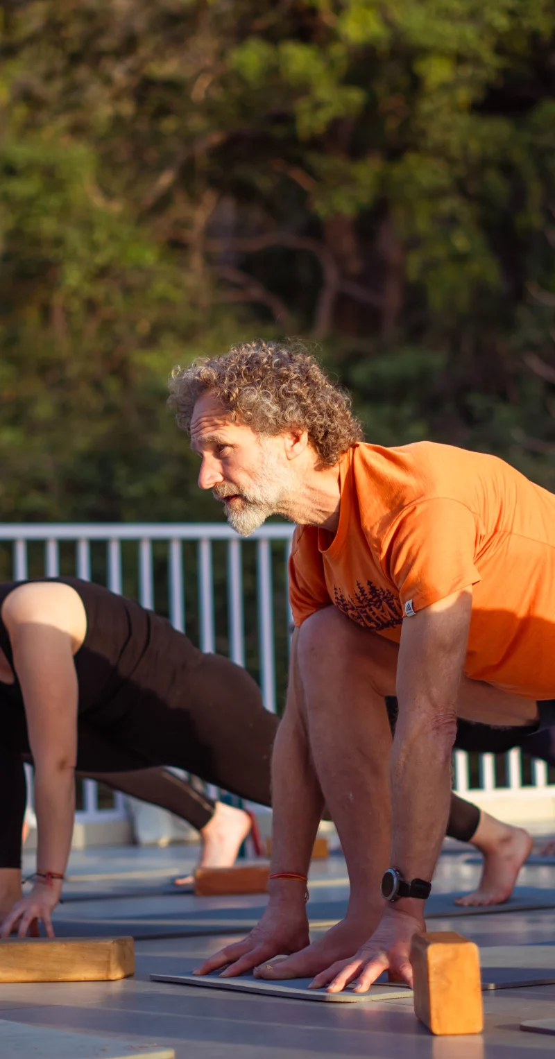 An older man in a low lunge on a rooftop yoga deck