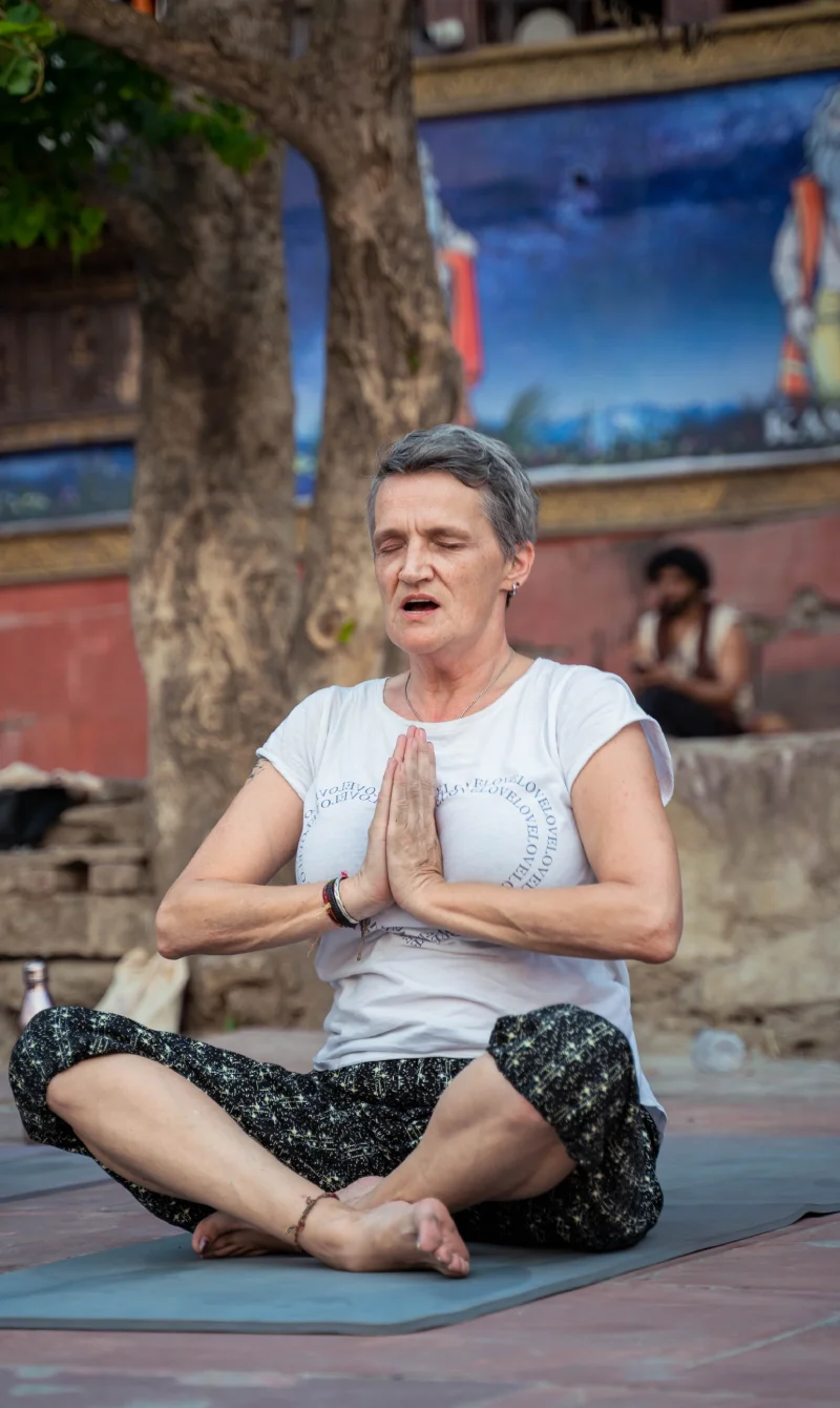 An older woman chanting with palms joined on a mat by the ghats