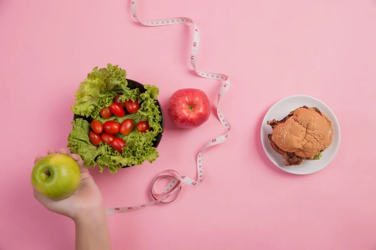 A salad bowl, an apple, and a tape measure on a pink table