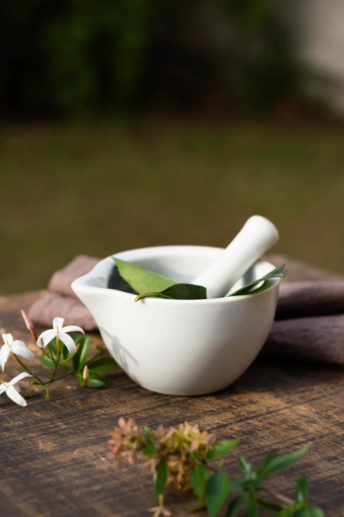 A mortar and pestle with fresh herbs and jasmine flowers