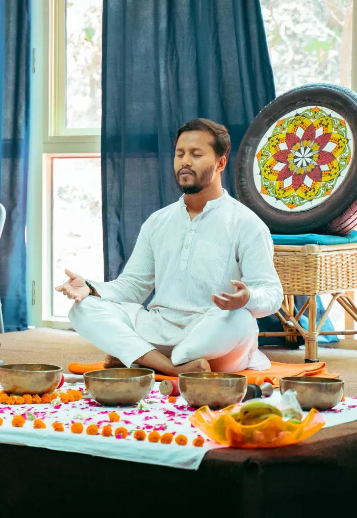 A teacher meditating beside singing bowls and flower offerings
