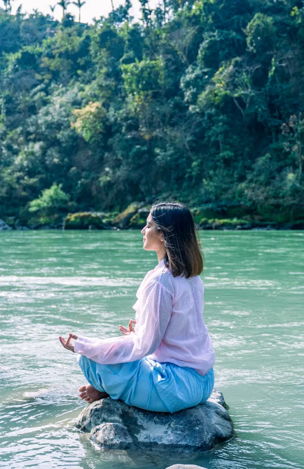 A woman meditating on a rock in the middle of the Ganges