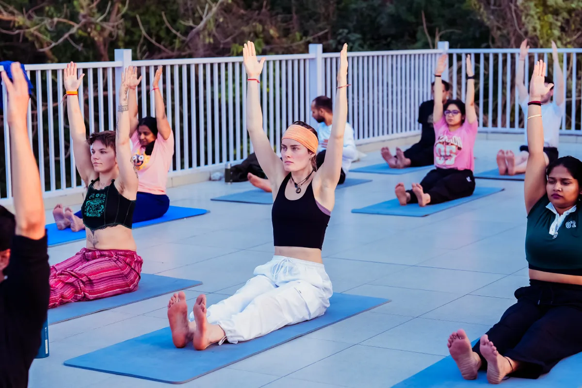 A group seated on mats with arms raised during a rooftop yoga class