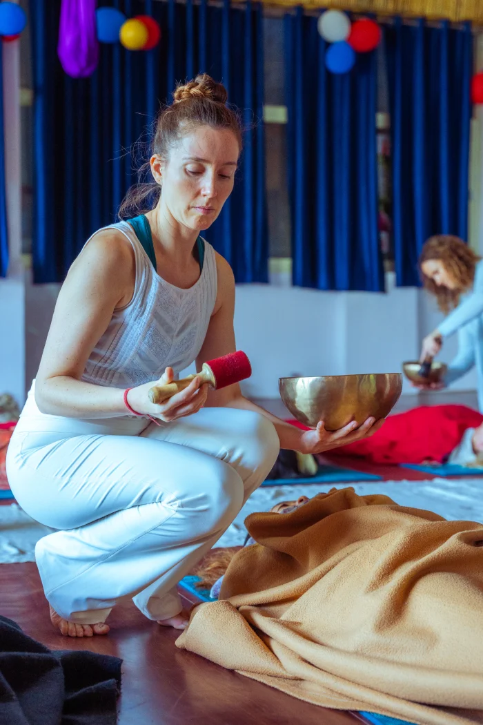 A teacher playing a singing bowl beside a student resting under a blanket