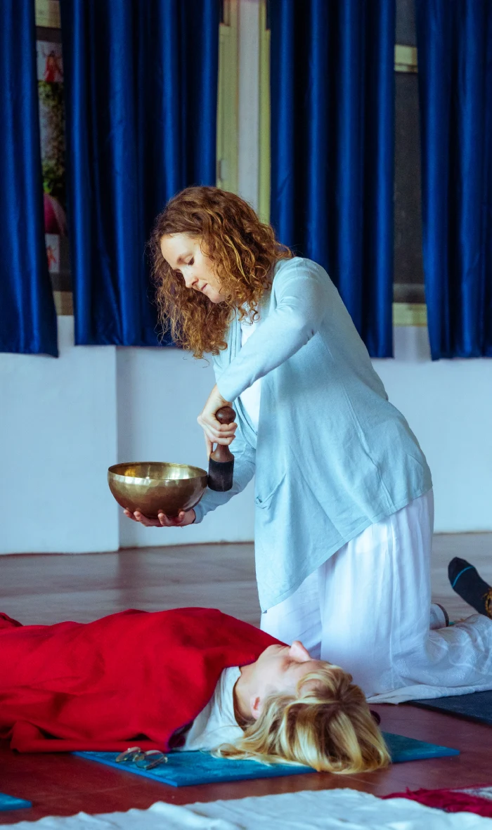 A teacher kneeling with a singing bowl beside a resting student