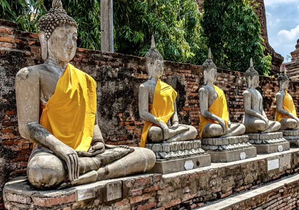 A row of seated Buddha statues draped in saffron cloth at an ancient temple