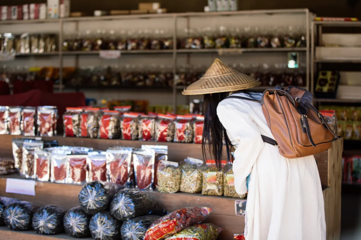 A traveller in a straw hat browsing dried goods at a local market stall