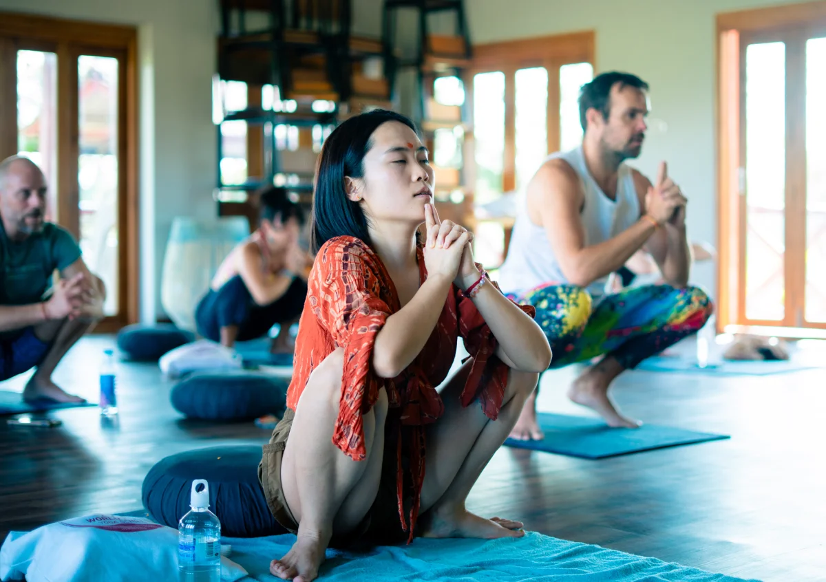 Students in a deep squat with hands joined at the chin during a kundalini class