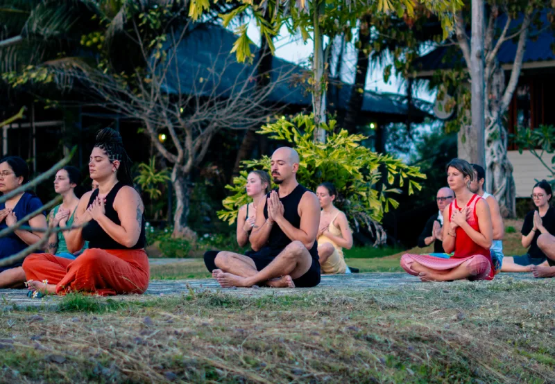Students meditating with joined palms on the lawn at the Chiang Mai school at dusk
