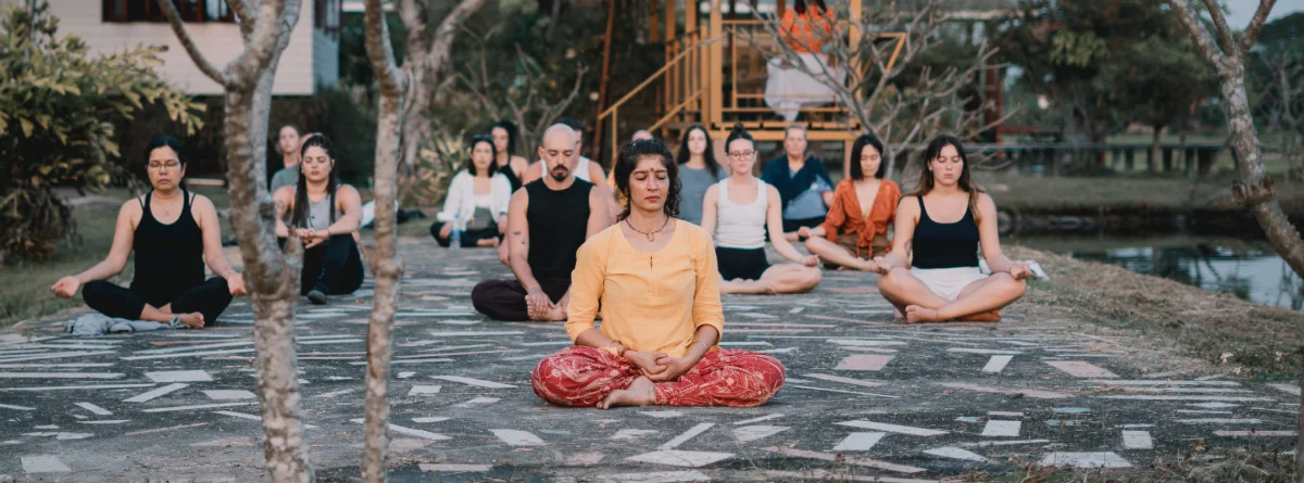 A group meditating cross-legged outdoors beside the pond in Chiang Mai